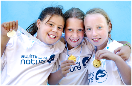 Three young girls holding medals wearing Swimming Nature t-shirts